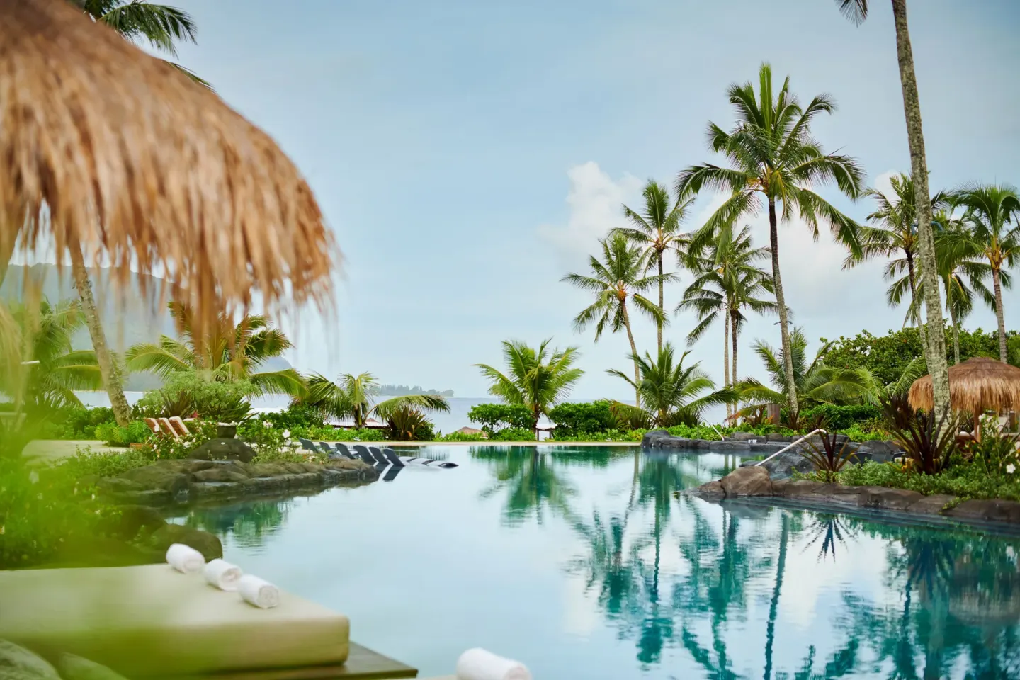 Lagoon-style pool with palms, loungers and ocean beyond at 1 Hotel Hanalei Bay.