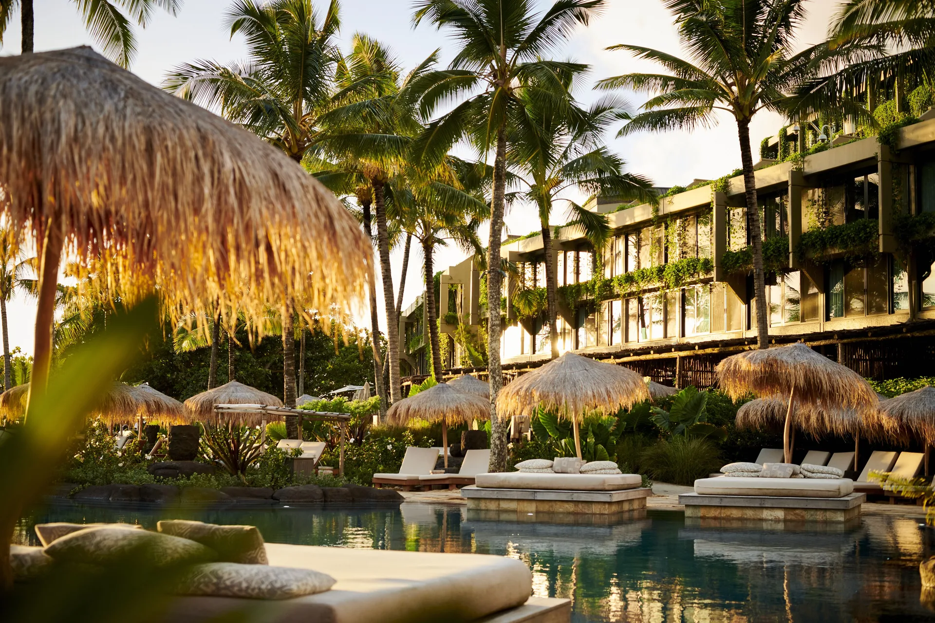 Poolside daybeds and thatched umbrellas among palms at 1 Hotel Hanalei Bay.