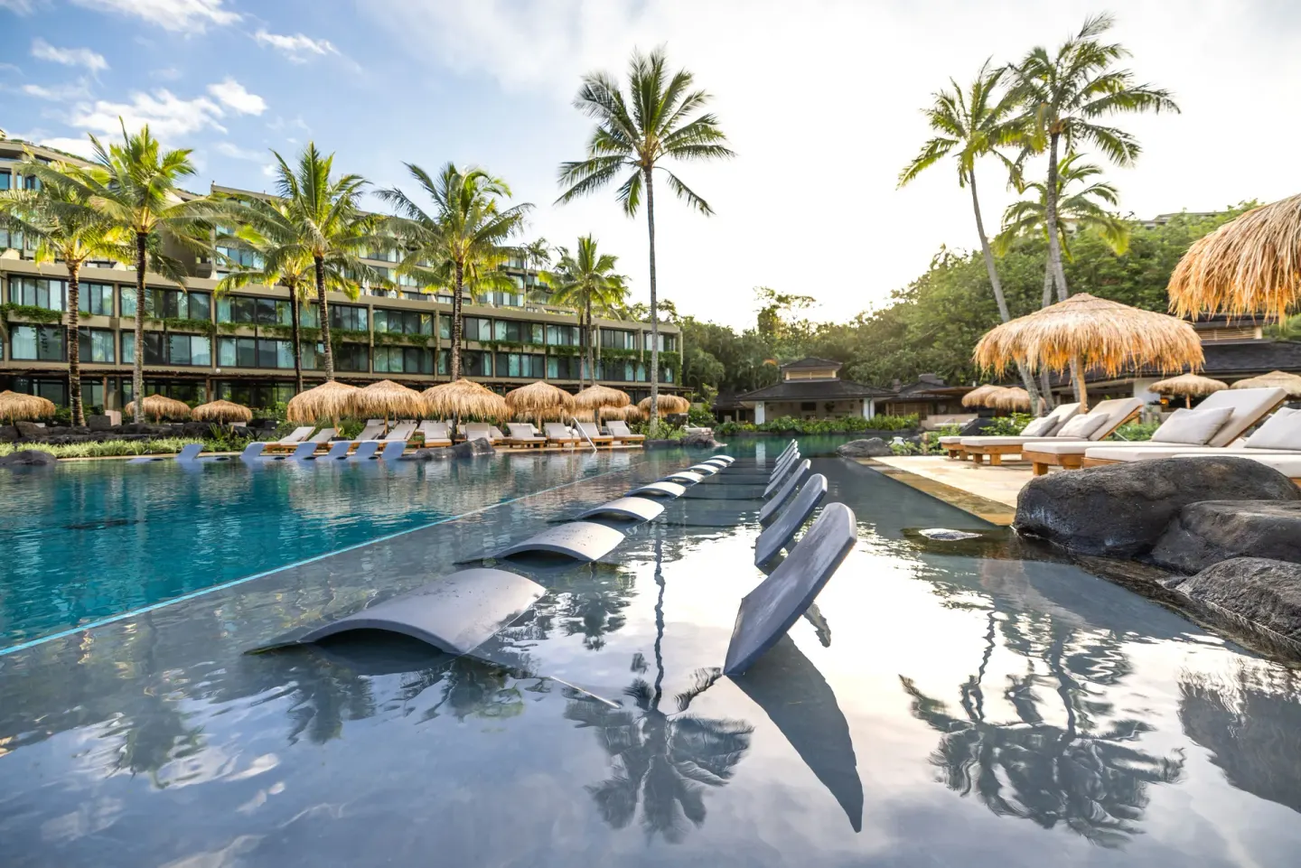 Resort pool with in-water loungers, cabanas and palm trees at 1 Hotel Hanalei Bay.