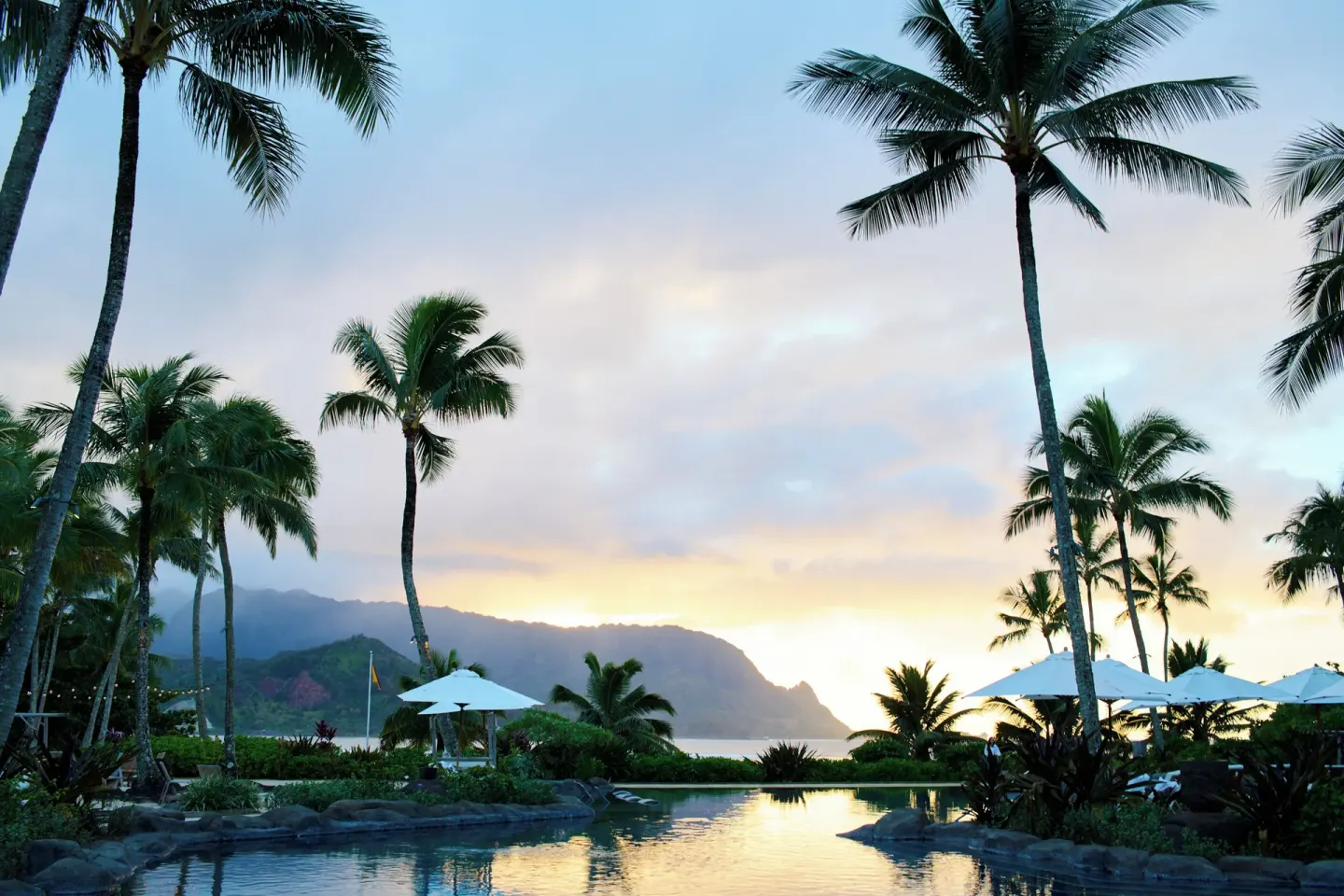 Sunset over a palm-framed pool and mountain shoreline at 1 Hotel Hanalei Bay.