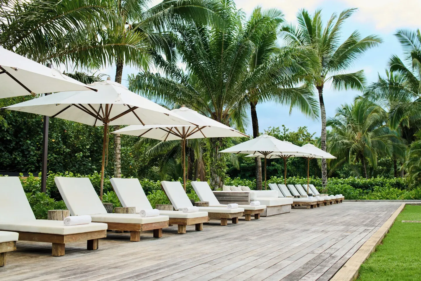 Lounge chairs and white umbrellas on a tropical deck at 1 Hotel Hanalei Bay.