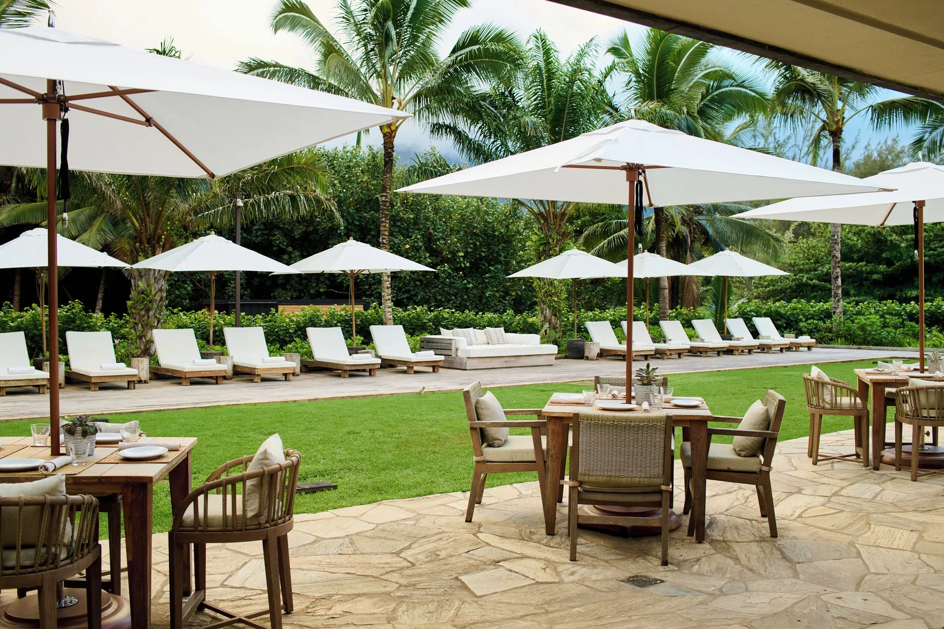 Outdoor dining tables beside a lounge chair lawn at 1 Hotel Hanalei Bay.