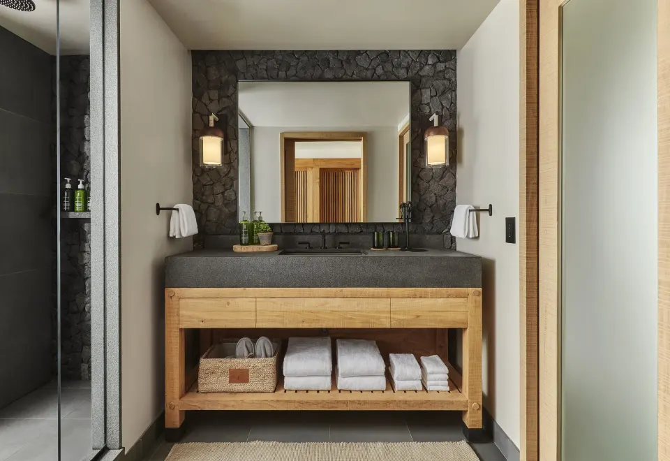 Mountain View bathroom vanity with stone wall, wood base, and folded towels at 1 Hotel Hanalei Bay.