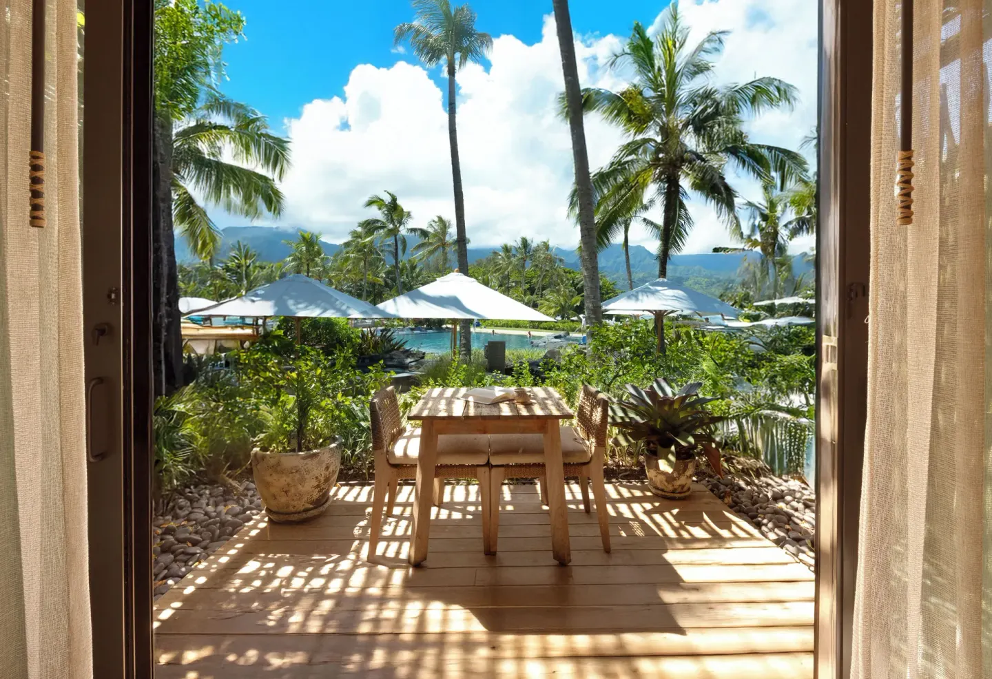 Room terrace at 1 Hotel Hanalei Bay with dining set, umbrellas, palms, pool and mountain views.