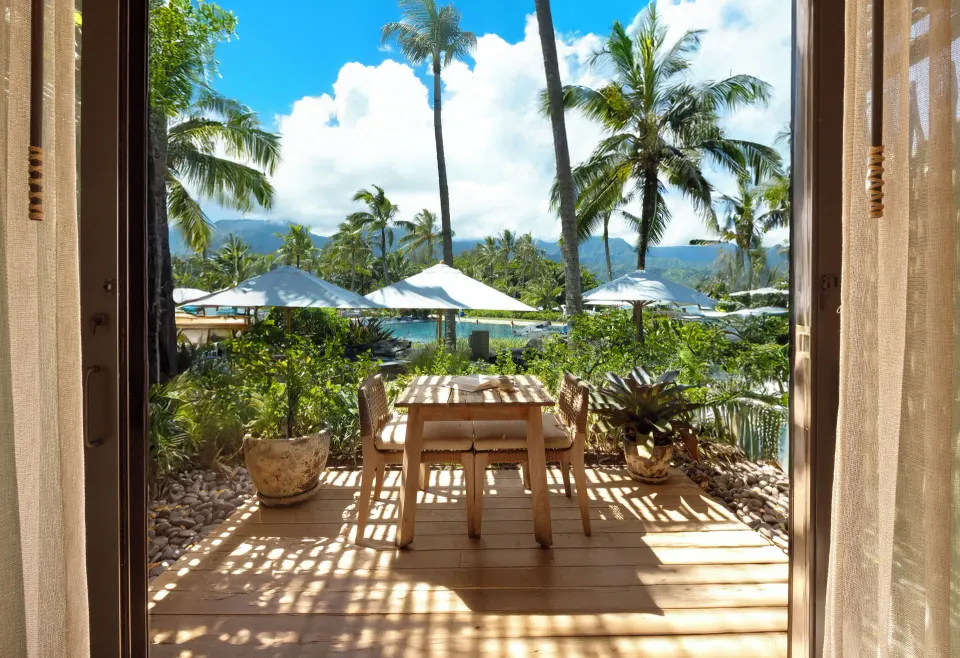 Room terrace at 1 Hotel Hanalei Bay with dining set, umbrellas, palms, pool and mountain views.