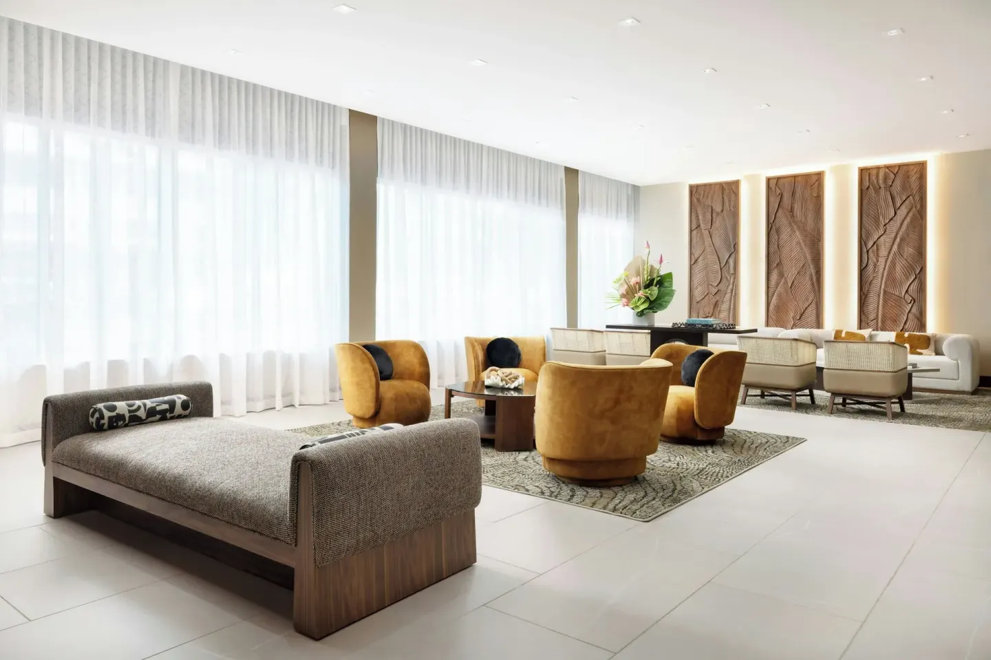 Bright lobby lounge with large windows, daybed, chairs, and sofas at AC Hotel Honolulu.