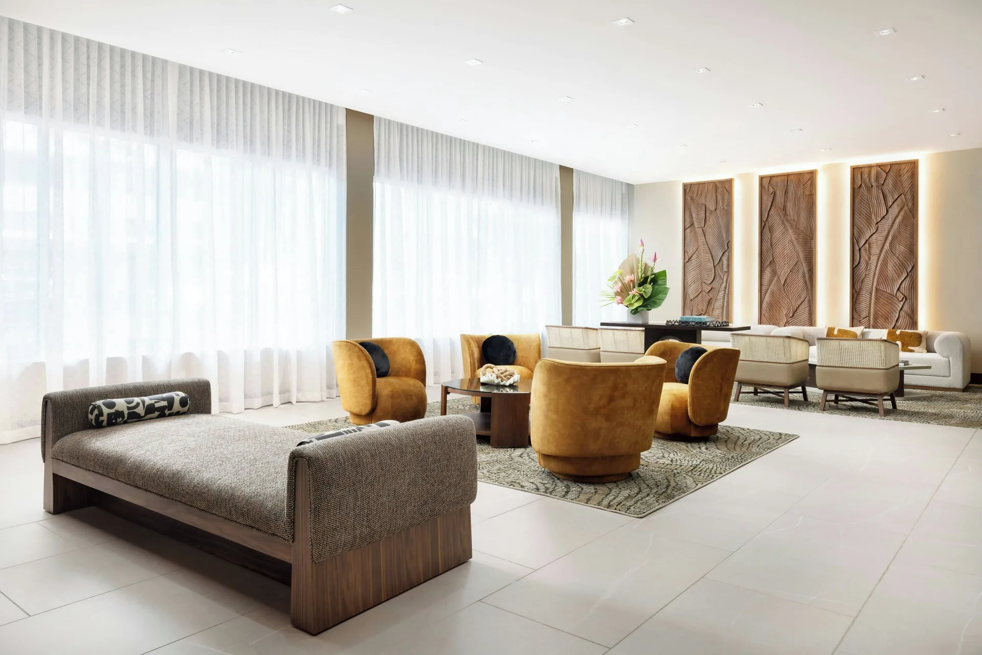 Bright lobby lounge with large windows, daybed, chairs, and sofas at AC Hotel Honolulu.