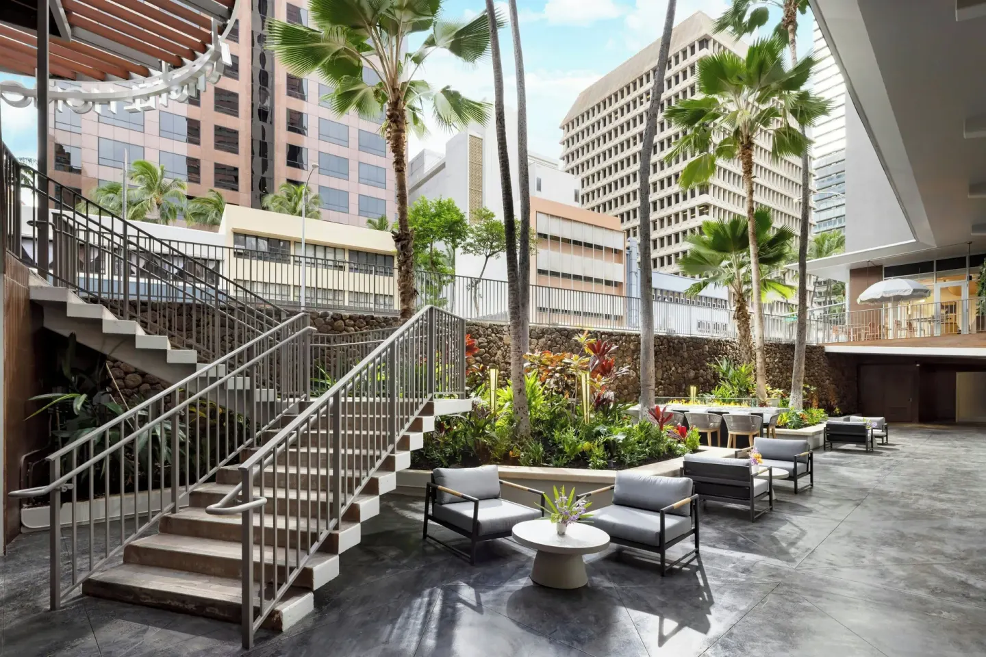 Open courtyard with stairs, lounge chairs, palms and city buildings at AC Hotel Honolulu.