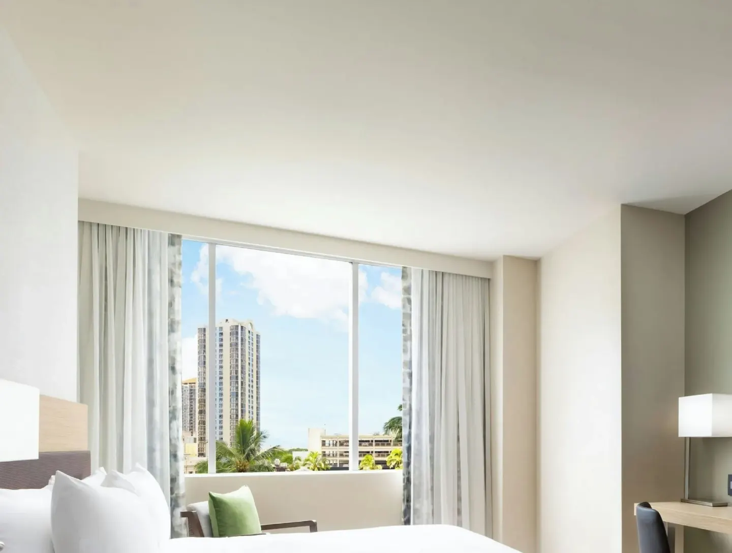 Guest room with bed, desk, lamp and city-view window at AC Hotel Honolulu.