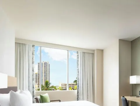 Guest room with bed, desk, lamp and city-view window at AC Hotel Honolulu.