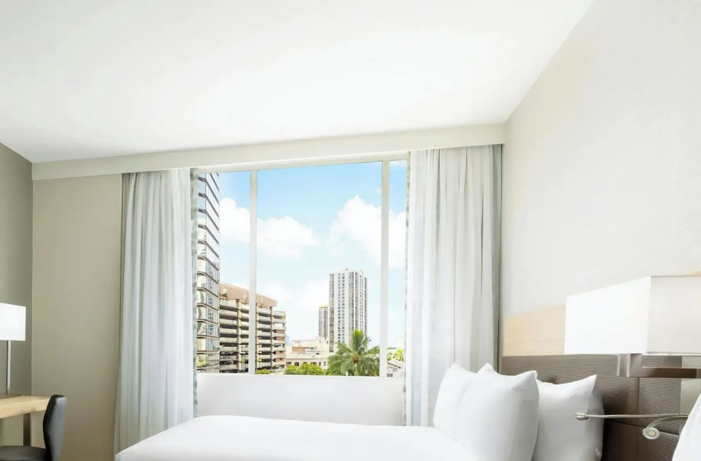 Guest room bed beside a large city-view window at AC Hotel Honolulu.