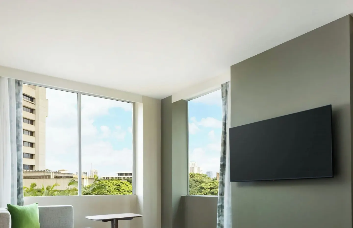 Guest room seating area and wall-mounted TV beside large windows at AC Hotel Honolulu.