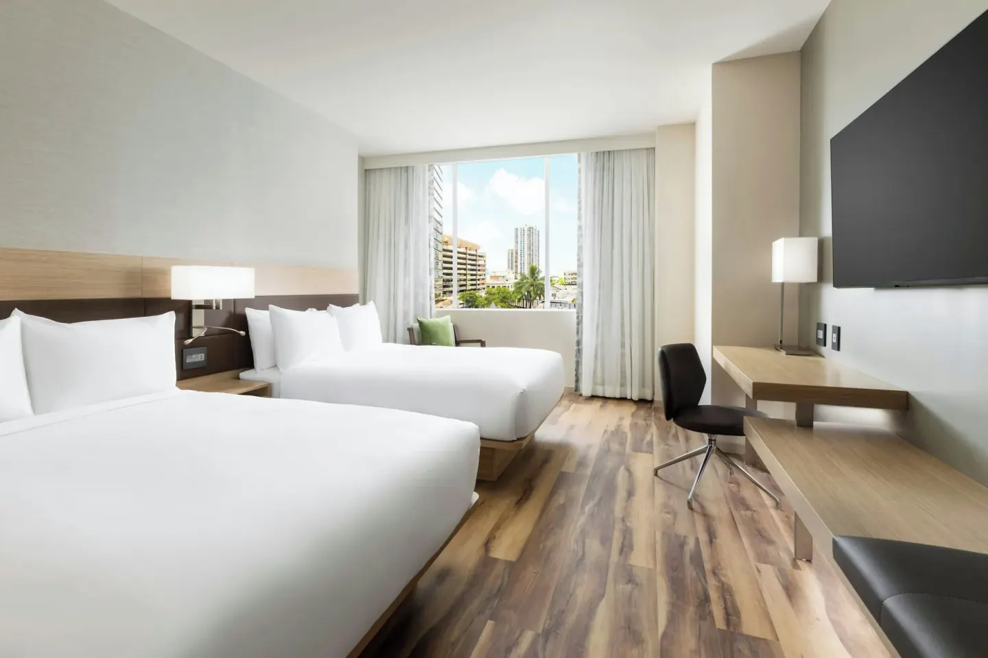 Guest room with two beds, desk, wall-mounted TV, and city-facing window at AC Hotel Honolulu.