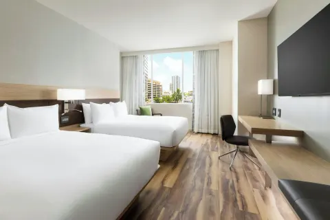 Guest room with two beds, desk, wall-mounted TV, and city-facing window at AC Hotel Honolulu.