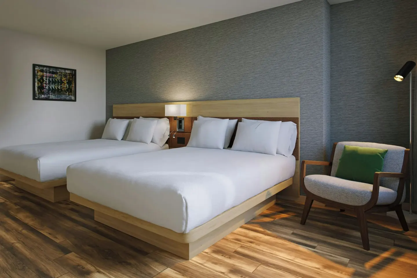 Guest room with two beds, wood flooring, lounge chair, and gray accent wall at AC Hotel Honolulu.