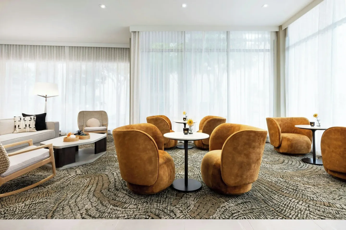 Lobby lounge with amber chairs, round tables, and sheer curtains at AC Hotel Honolulu.