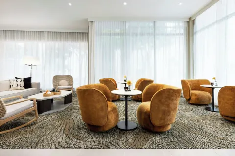Lobby lounge with amber chairs, round tables, and sheer curtains at AC Hotel Honolulu.