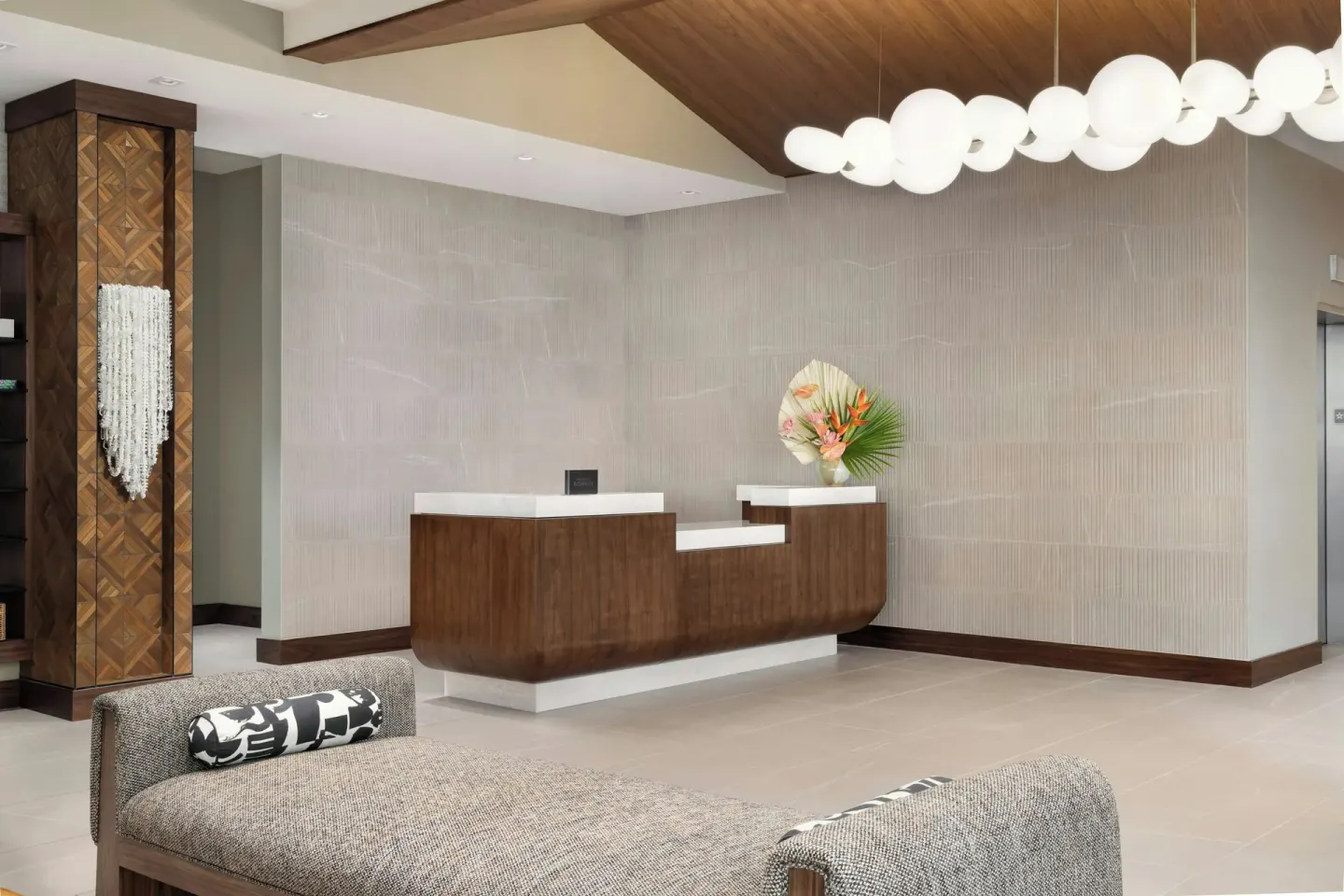 Reception desk with wood finishes and sculptural lighting in the lobby at AC Hotel Honolulu.
