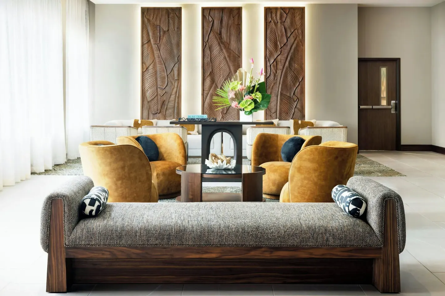 Lobby seating with lounge chairs, carved wall panels, and flowers at AC Hotel Honolulu.