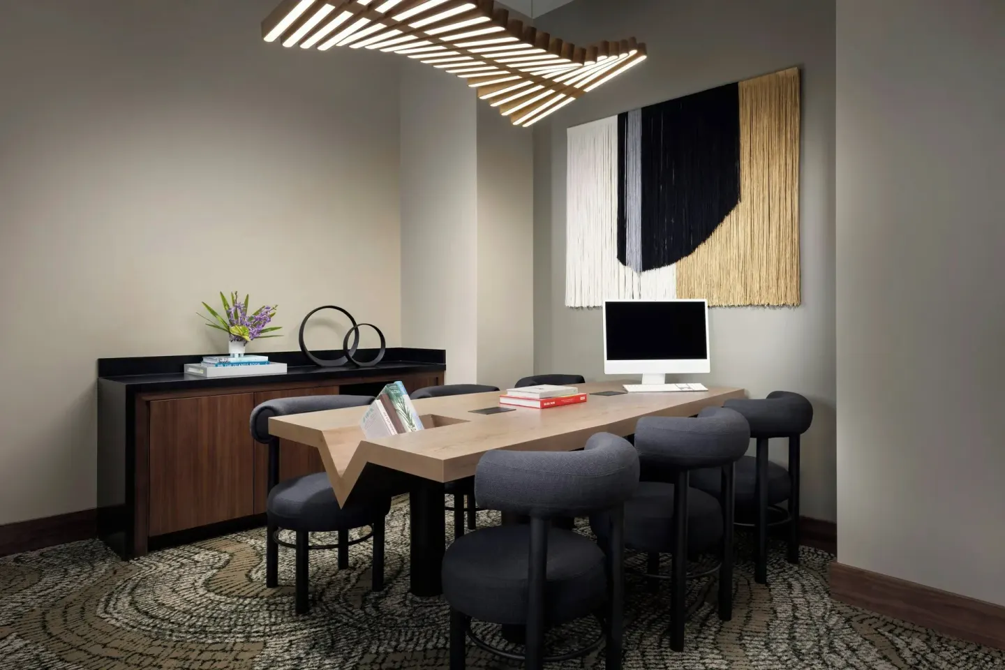 Work table with computer, stools, wall art and sculptural ceiling light at AC Hotel Honolulu.