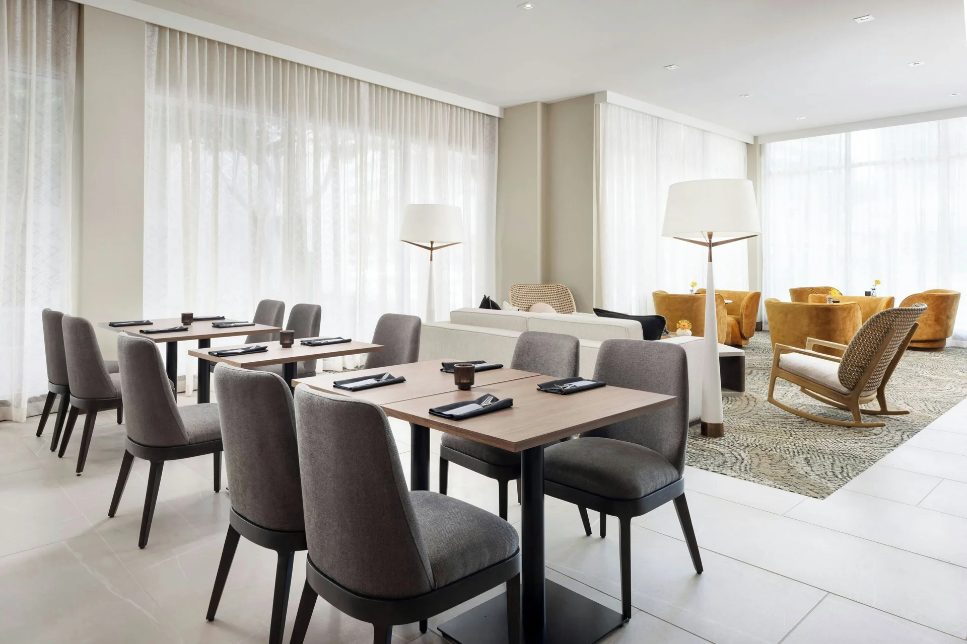 Dining tables beside a lounge area with yellow chairs at AC Hotel Honolulu.