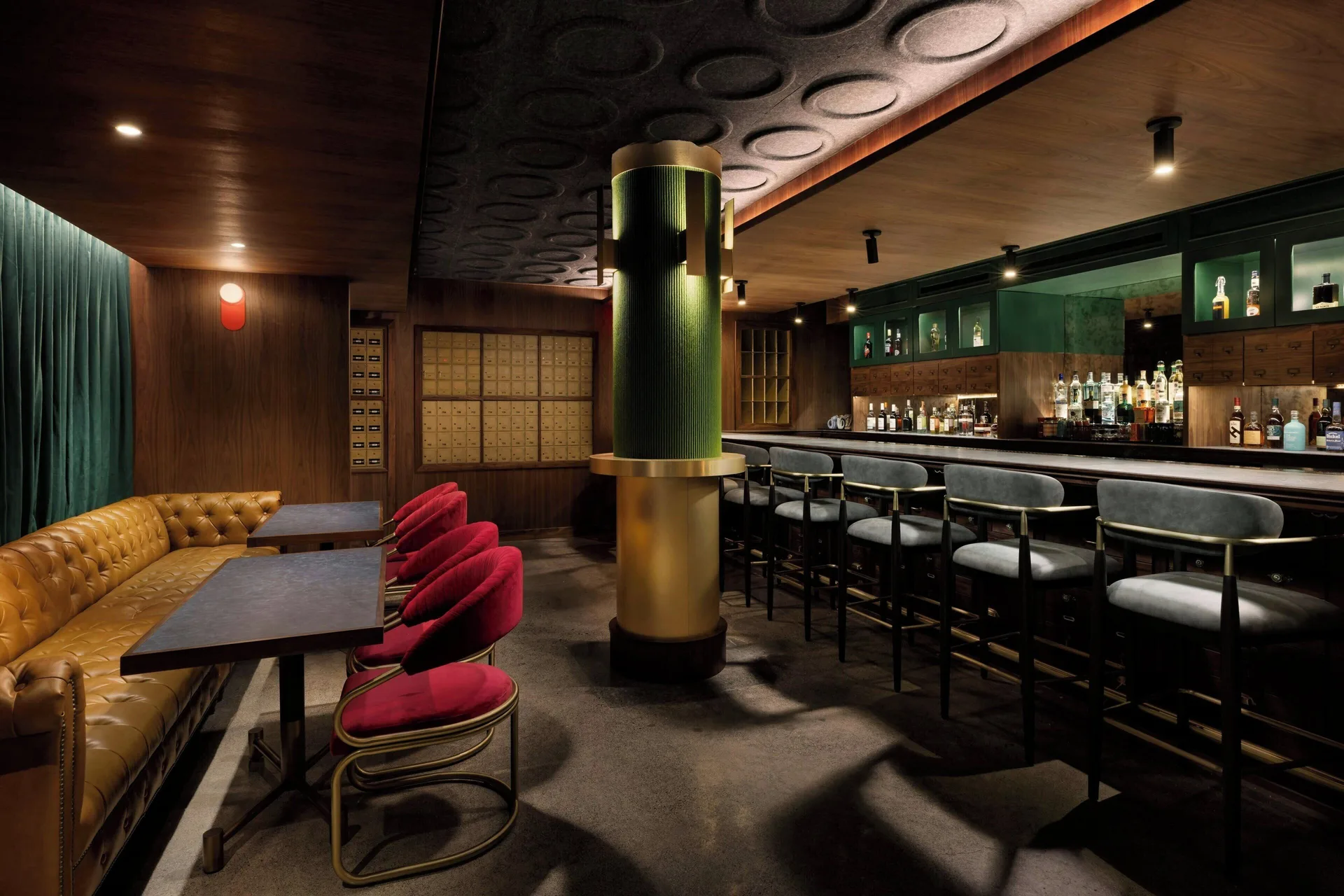 Dim cocktail bar with red chairs and leather banquette at AC Hotel Honolulu.