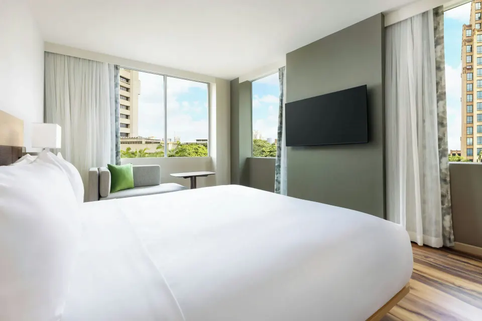 City View king room with bed, TV wall, sofa, and corner windows at AC Hotel Honolulu.