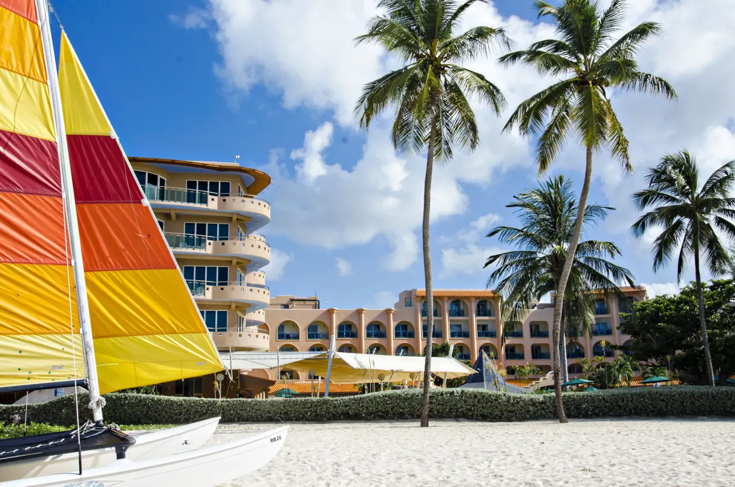 Beachfront hotel buildings, palm trees, and a sailboat at Accra Beach Hotel & Spa.
