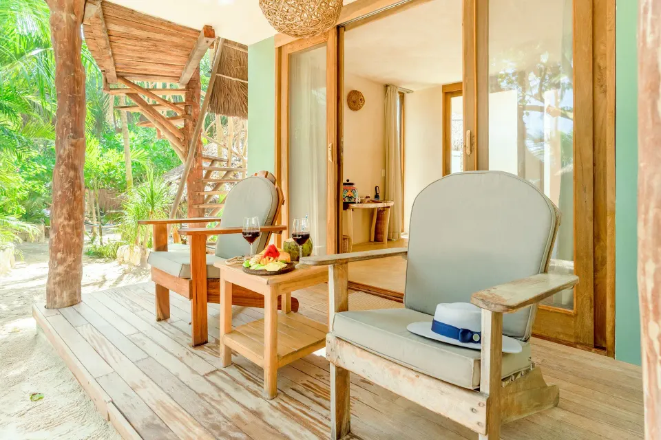 Sunlit wooden terrace with two chairs and fruit plate at Ahau Tulum