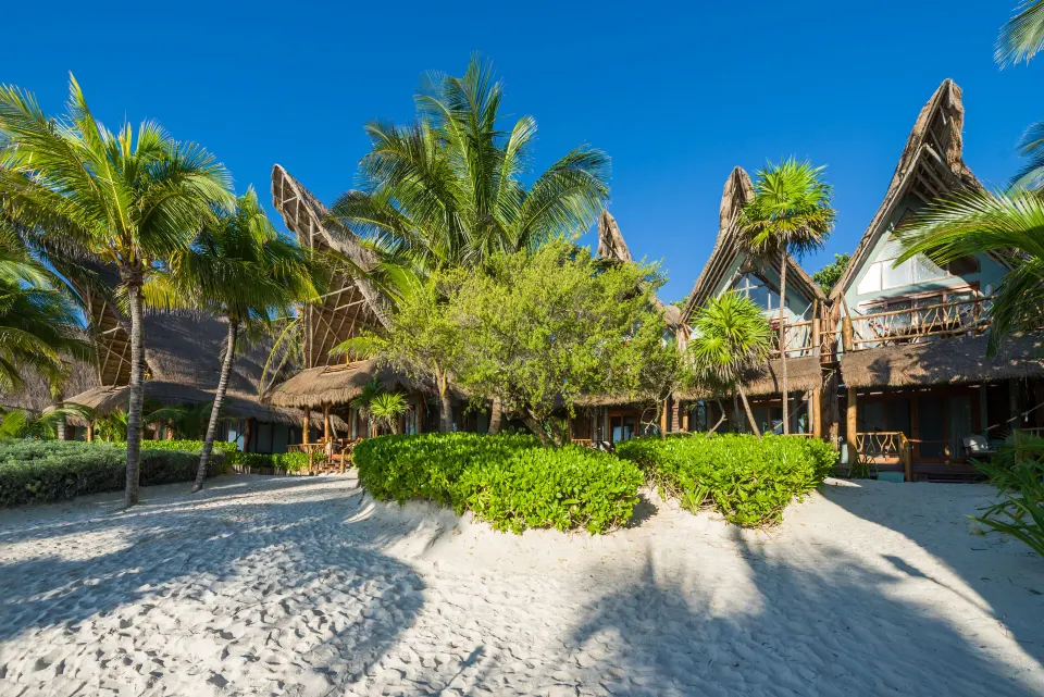 Thatched-roof resort buildings and landscaped beach area at Ahau Tulum
