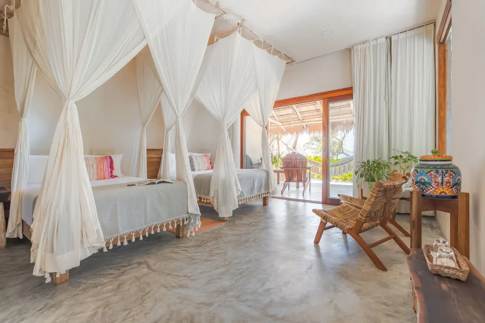 Twin canopy beds and a wooden chair opening to a balcony at Ahau Tulum