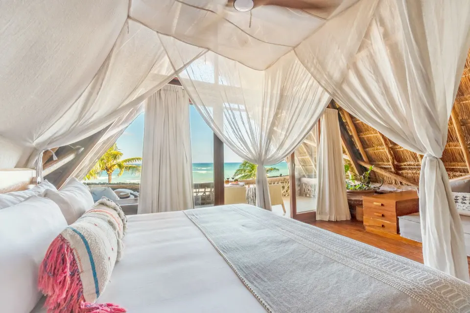 Canopy bed with view of the ocean through balcony doors in a guest room at Ahau Tulum