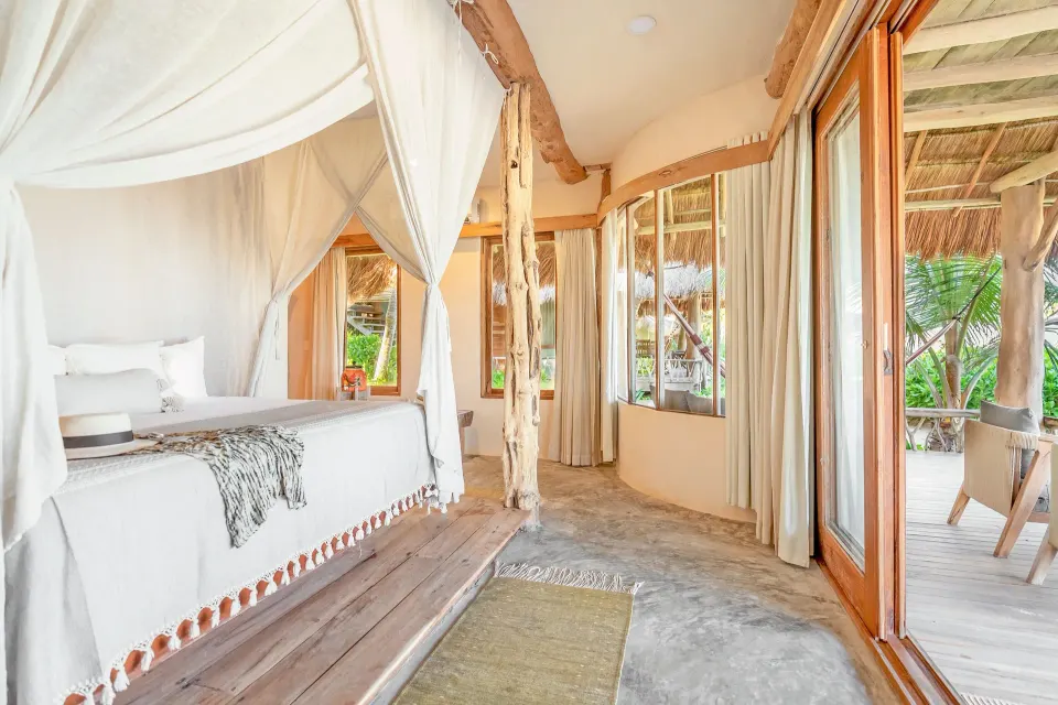 Canopy king bed and sliding doors open to a tropical patio at Ahau Tulum