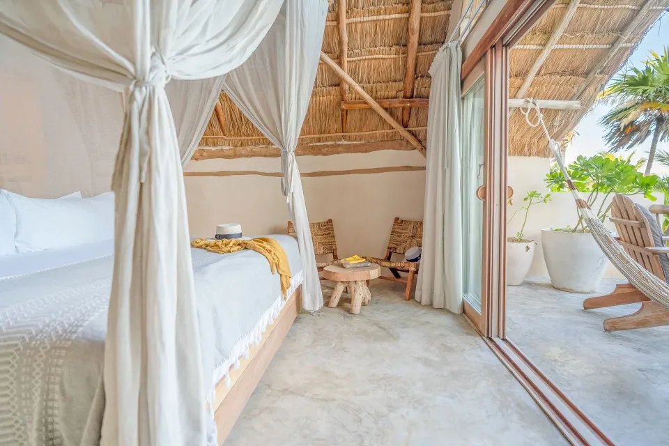 Canopy king bed with thatched roof and sliding doors to a private terrace at Ahau Tulum