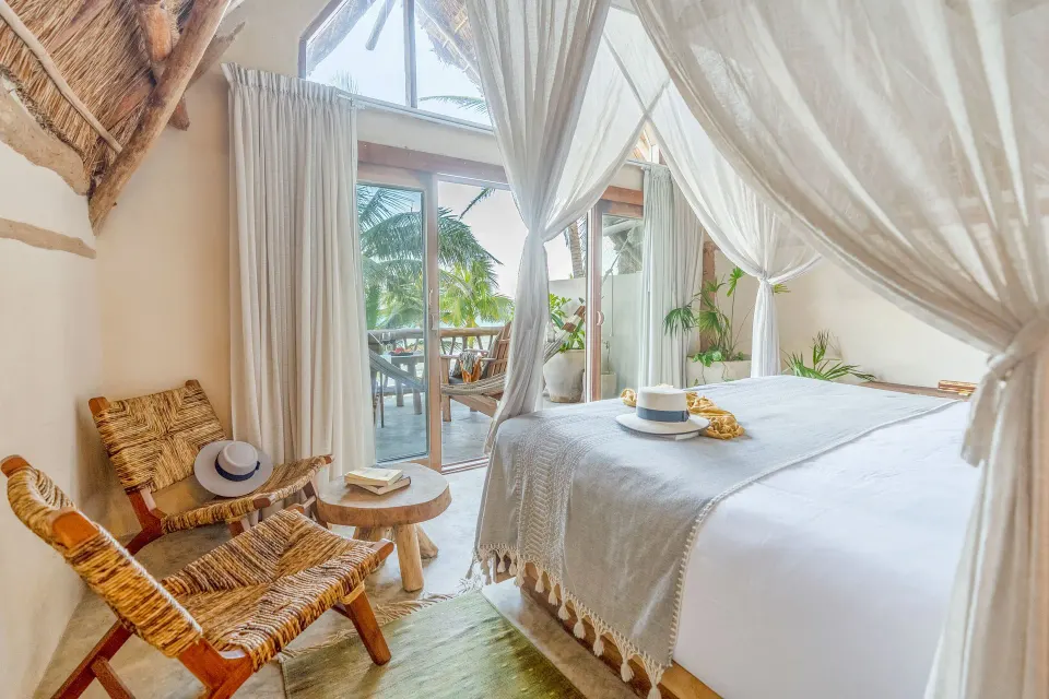 Canopy bed and woven chairs beside glass doors to a balcony at Ahau Tulum