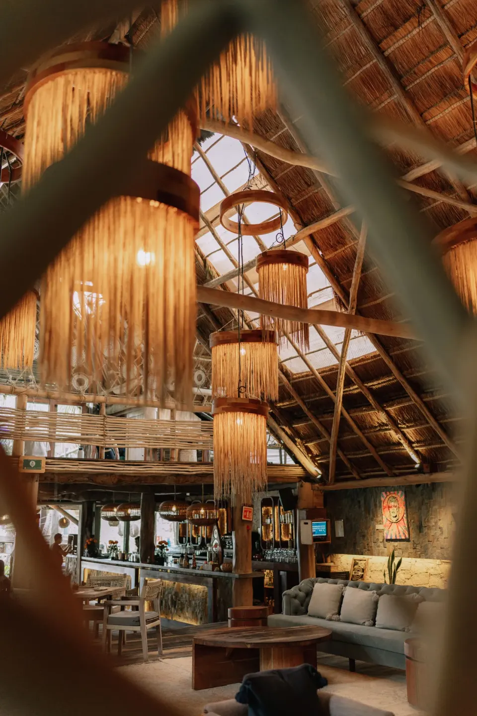 Close-up view of fringed pendant lights and bar seating through a decorative screen at Ahau Tulum