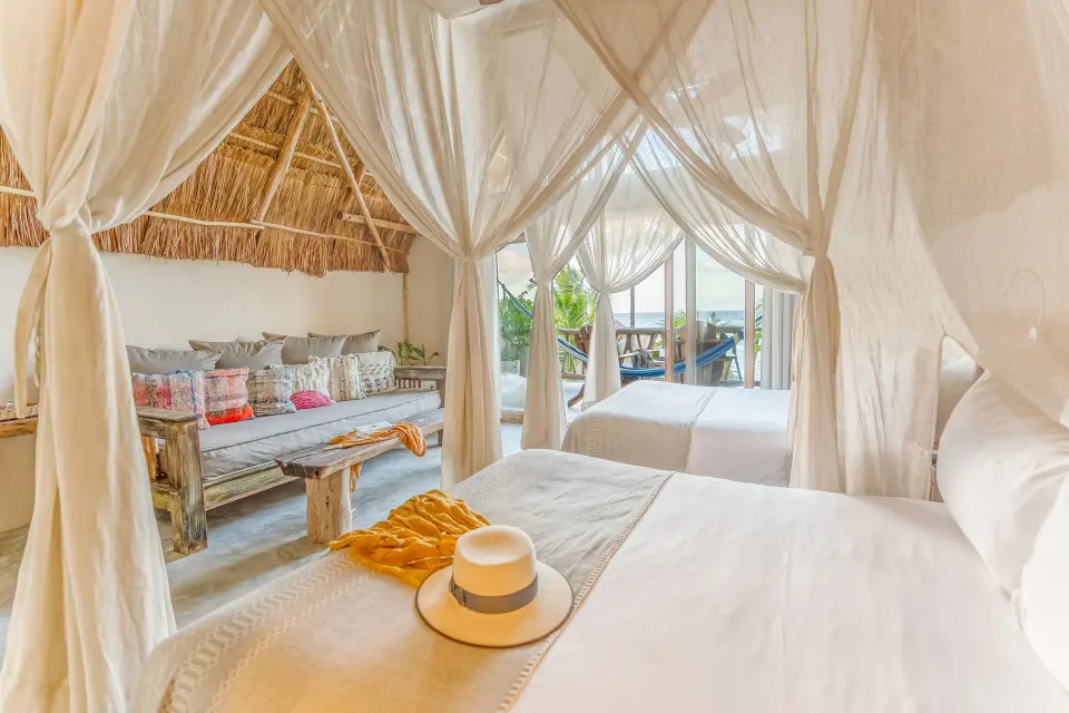 Canopied king bed and seating area in a palapa guest room at Ahau Tulum