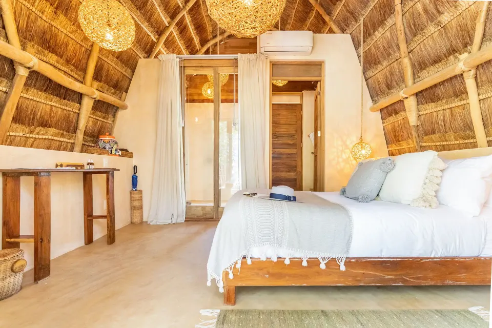 Open-plan palapa bedroom with king bed and rustic wood desk at Ahau Tulum