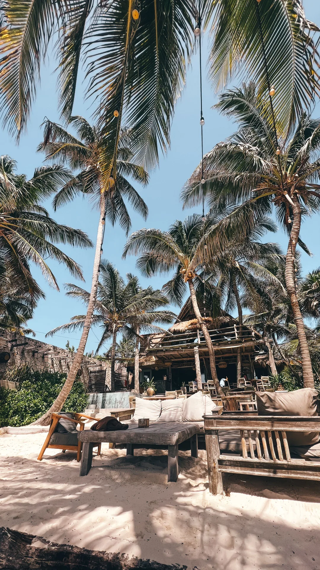 Tall palm trees framing beachfront seating and a thatched restaurant at Ahau Tulum.