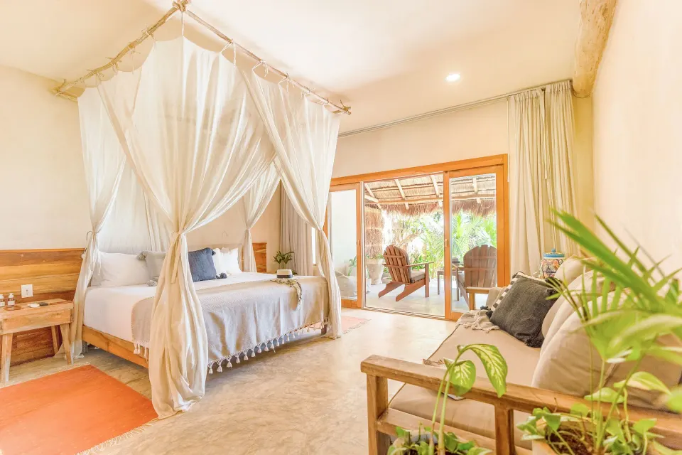 Bright suite with canopy bed and seating area opening to a porch at Ahau Tulum