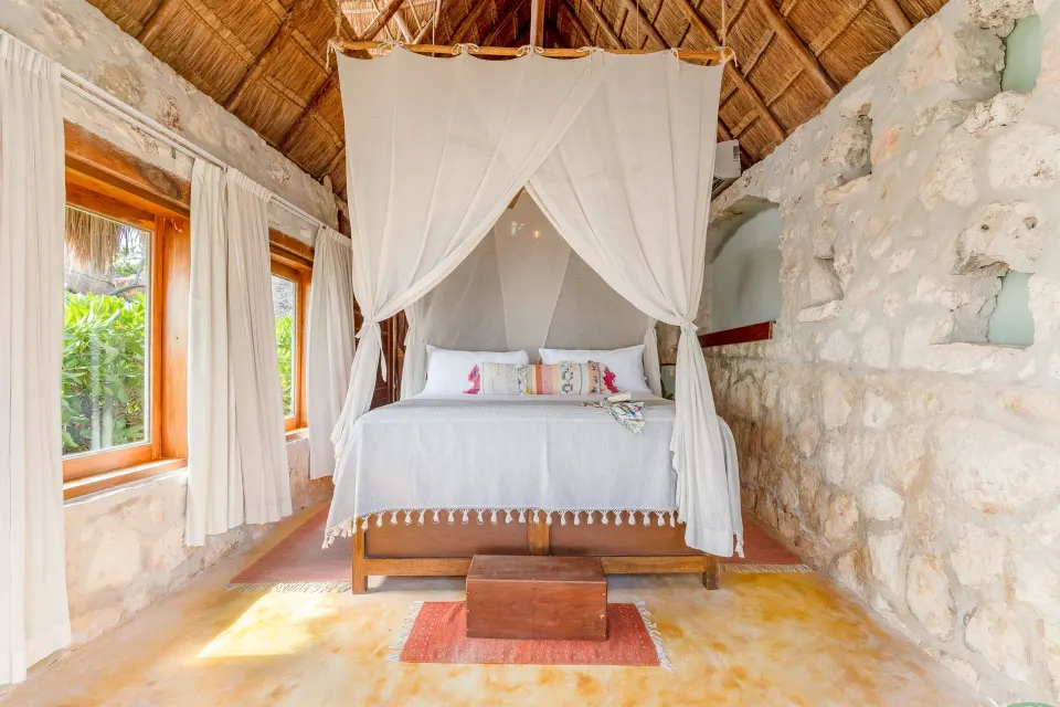 Stone-walled room with a canopy king bed and wooden windows at Ahau Tulum