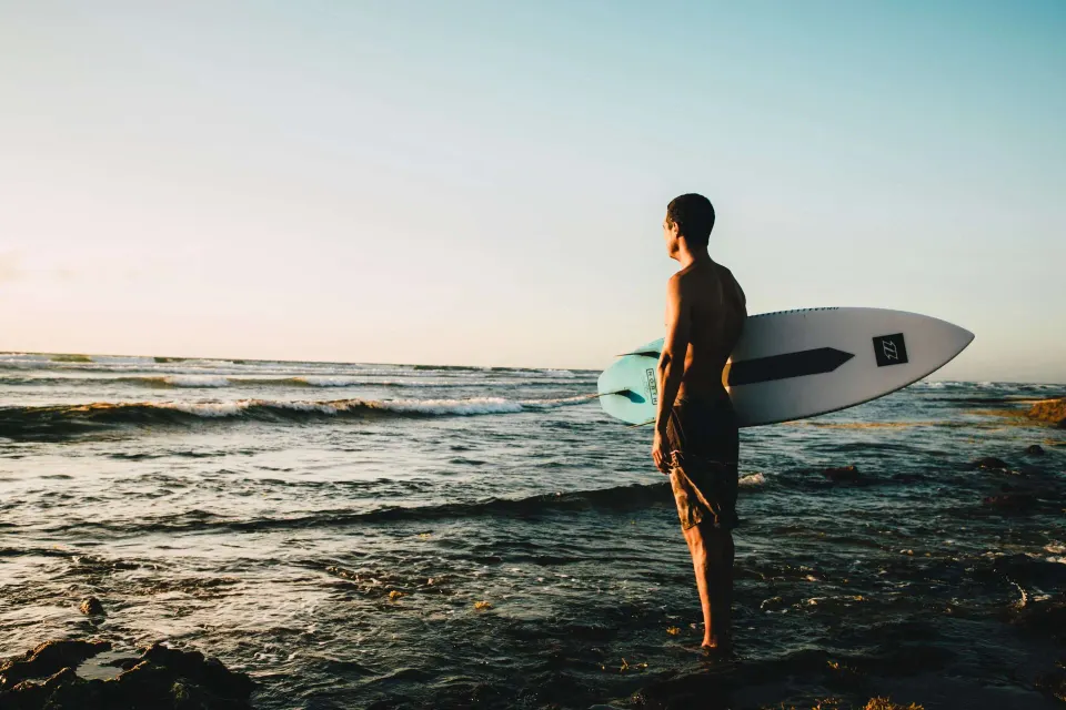 Surfer holding a board and looking out over the ocean at Ahau Tulum at sunset