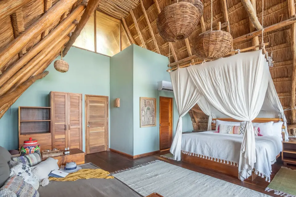 Thatched‑roof bedroom with king bed and wardrobe at Ahau Tulum