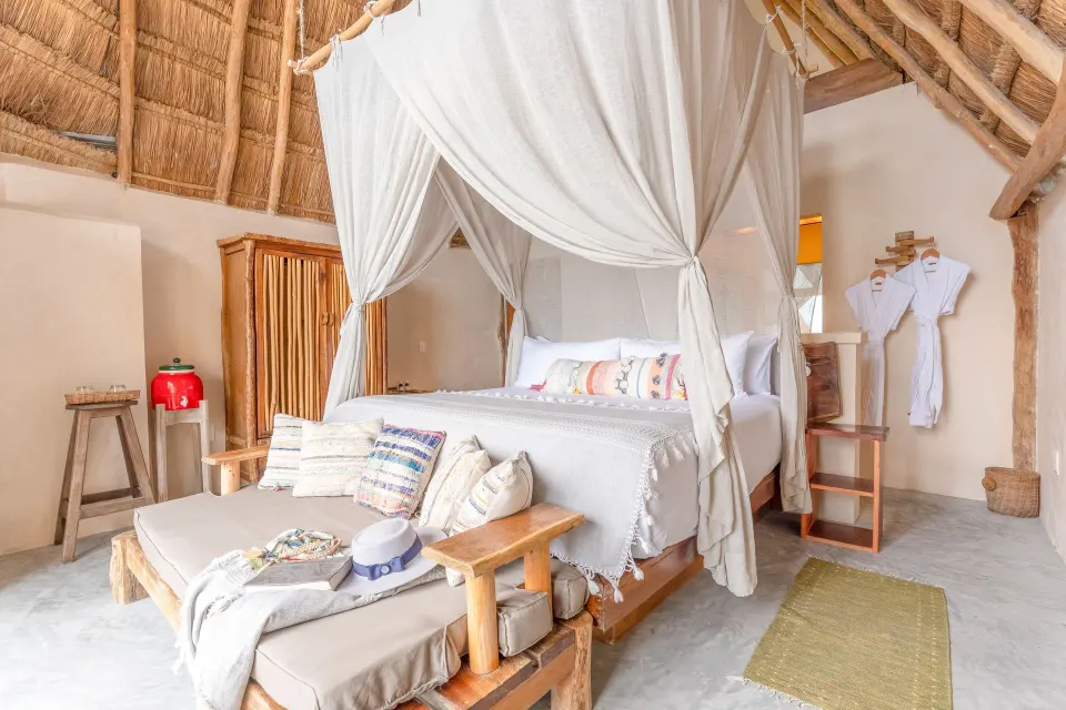 Thatched-roof canopy king bed with seating bench at Ahau Tulum