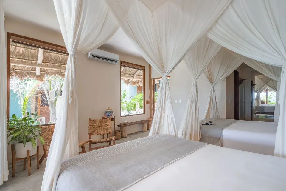 View across twin canopy beds toward a window in a palapa room at Ahau Tulum