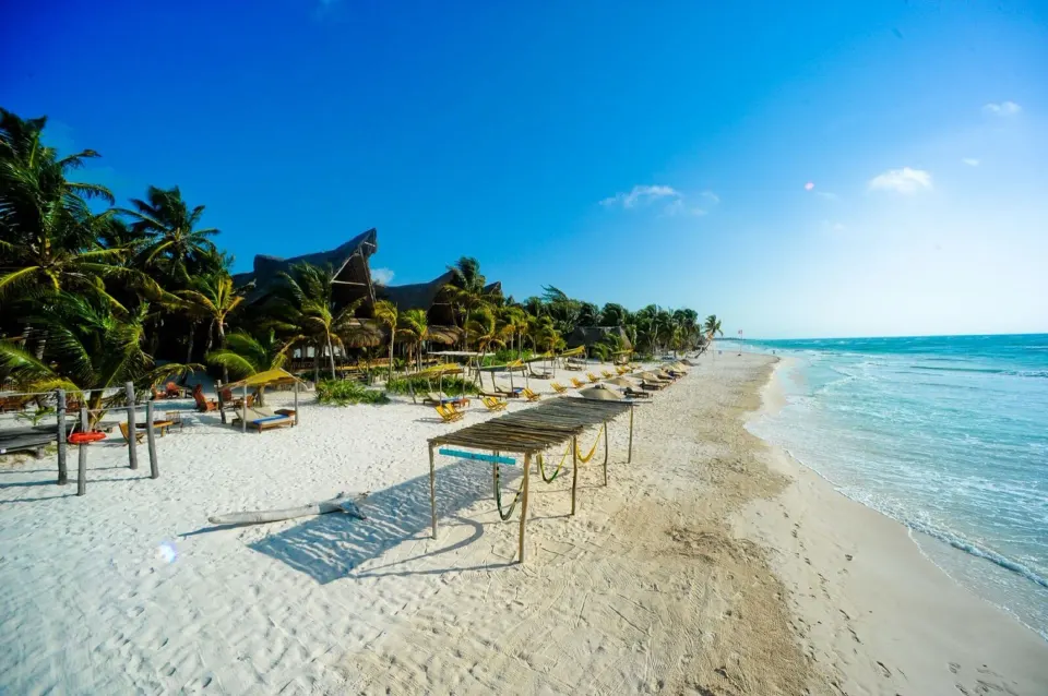 Wide sandy beach and turquoise sea with lounge huts at Ahau Tulum
