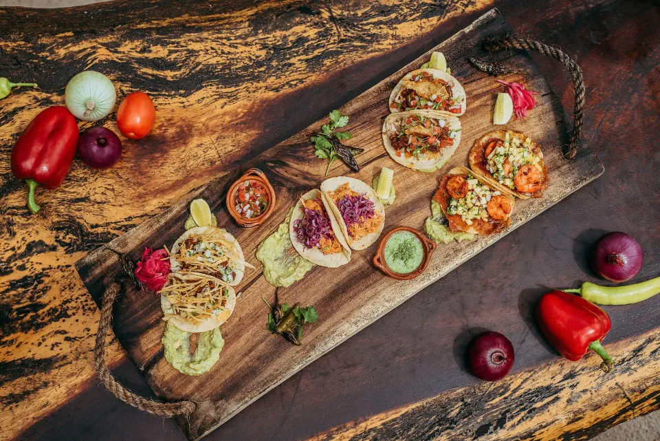 Assorted tacos and garnishes arranged on a wooden board at Ahau Tulum.