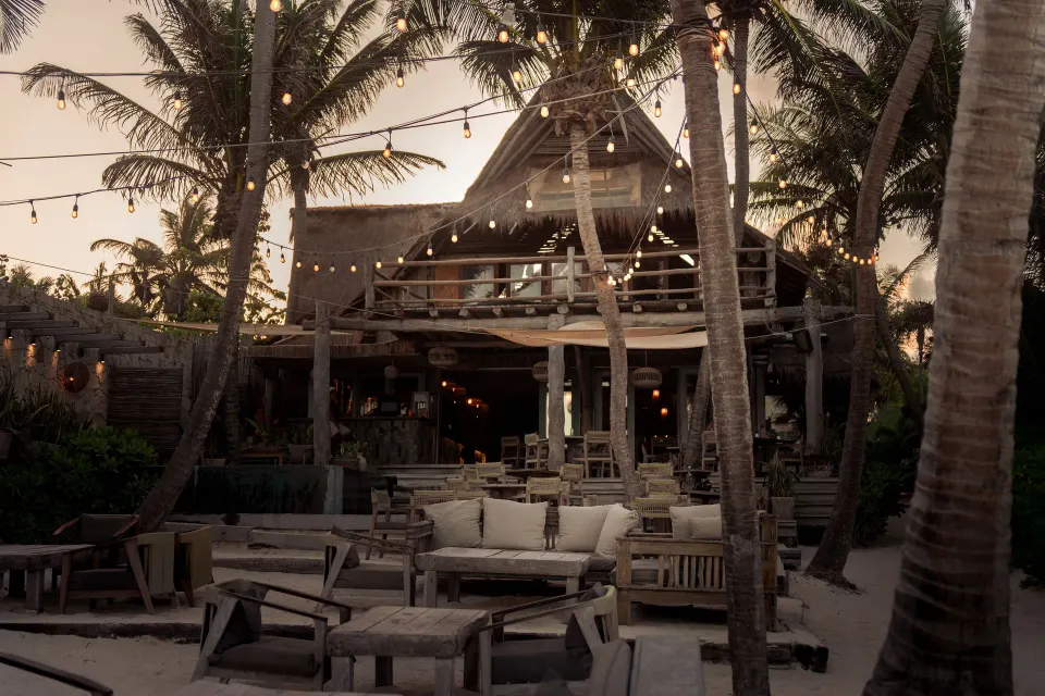 Outdoor beachfront lounge and bar area with string lights at Ahau Tulum