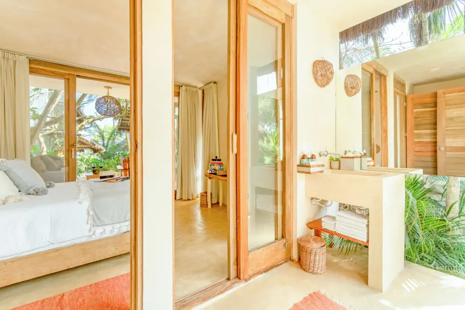 View from the bathroom into the bedroom of a Deluxe Room at Ahau Tulum showing towels and vanity items