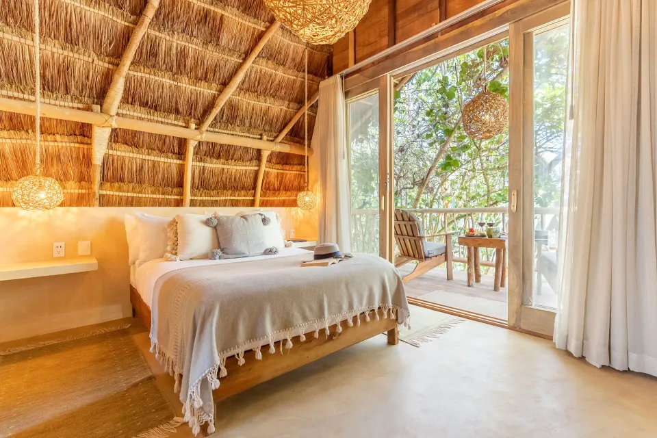 Bright Deluxe Room at Ahau Tulum with king bed and sliding doors to a tree-lined balcony